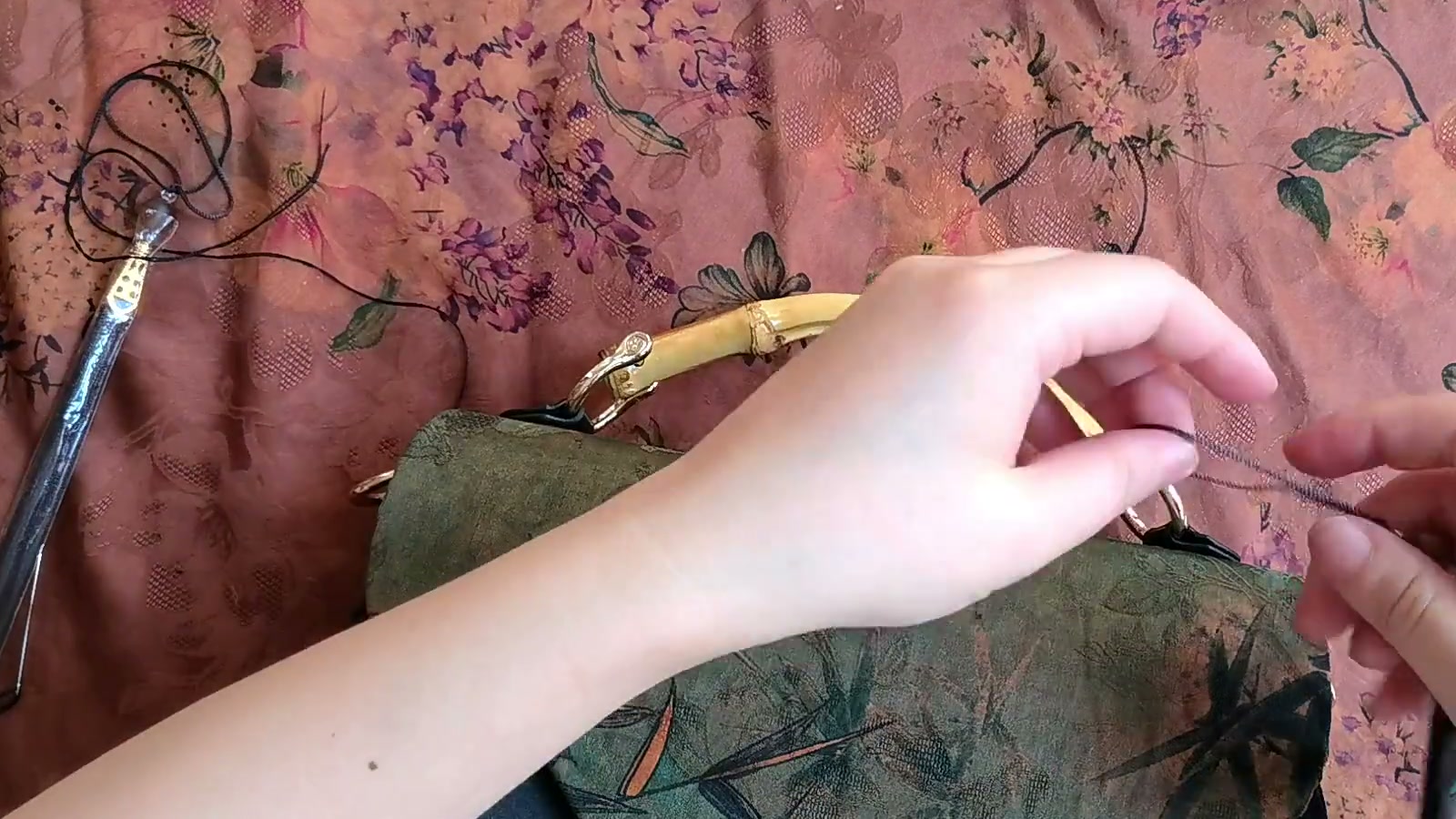 A hand clips the tassel charm onto the metal ring at the side of the finished handbag