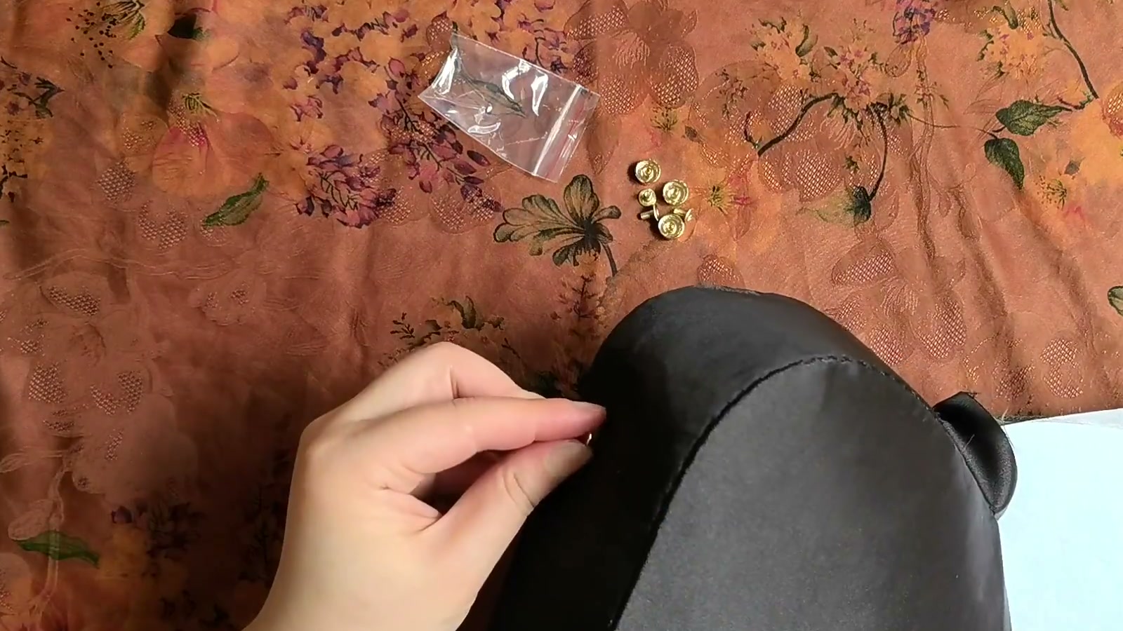 One gold screw-back bag foot is installed on the outside of the black bag base, with the remaining hardware nearby