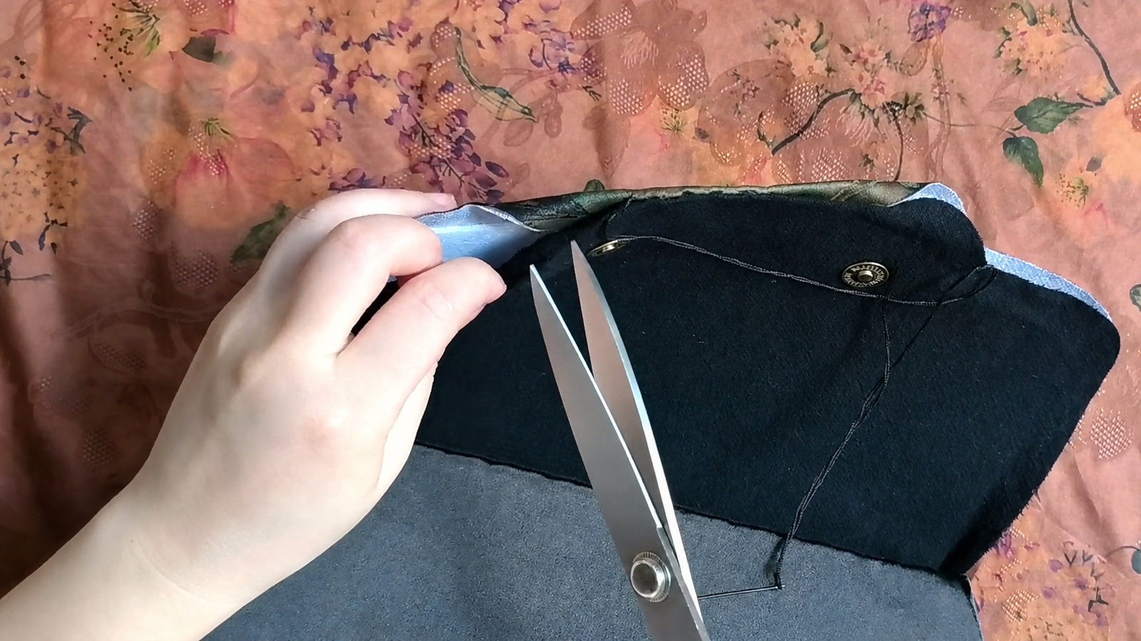 Scissors point toward the fabric seam allowance at the flap's inner curve while fingers fold the white batting safely away