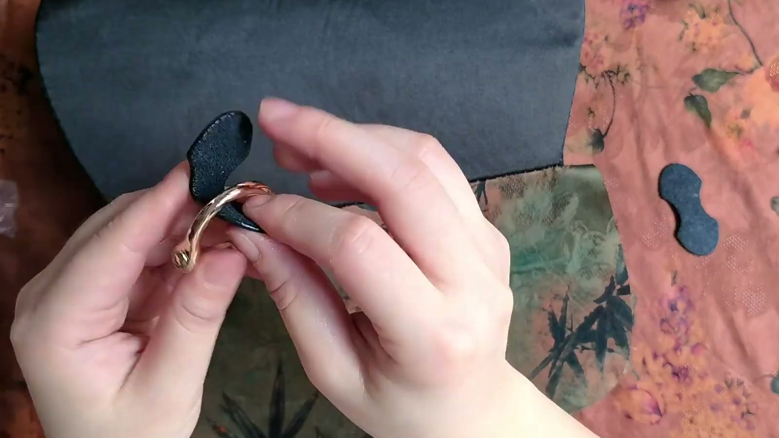 A black leather tab is folded around a gold U-ring before being aligned on the flap
