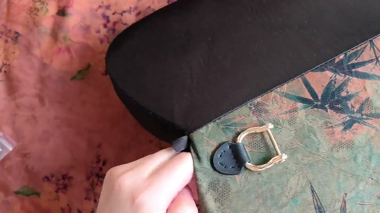 A hand needle sews through the pre-punched holes of a leather tab positioned on the floral flap