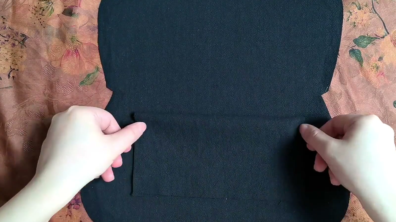The lower edge of a black lining pocket is flipped downward while fingers prepare it for stitching