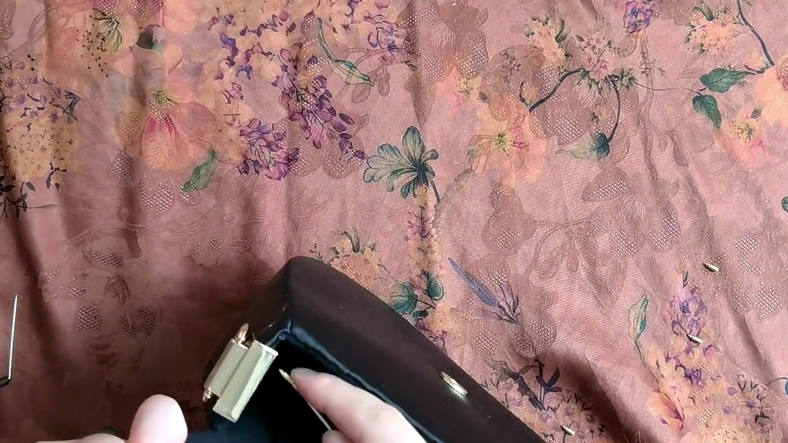 A metal side fitting clamps around the edge of the bag opening while a hand tightens its small screw