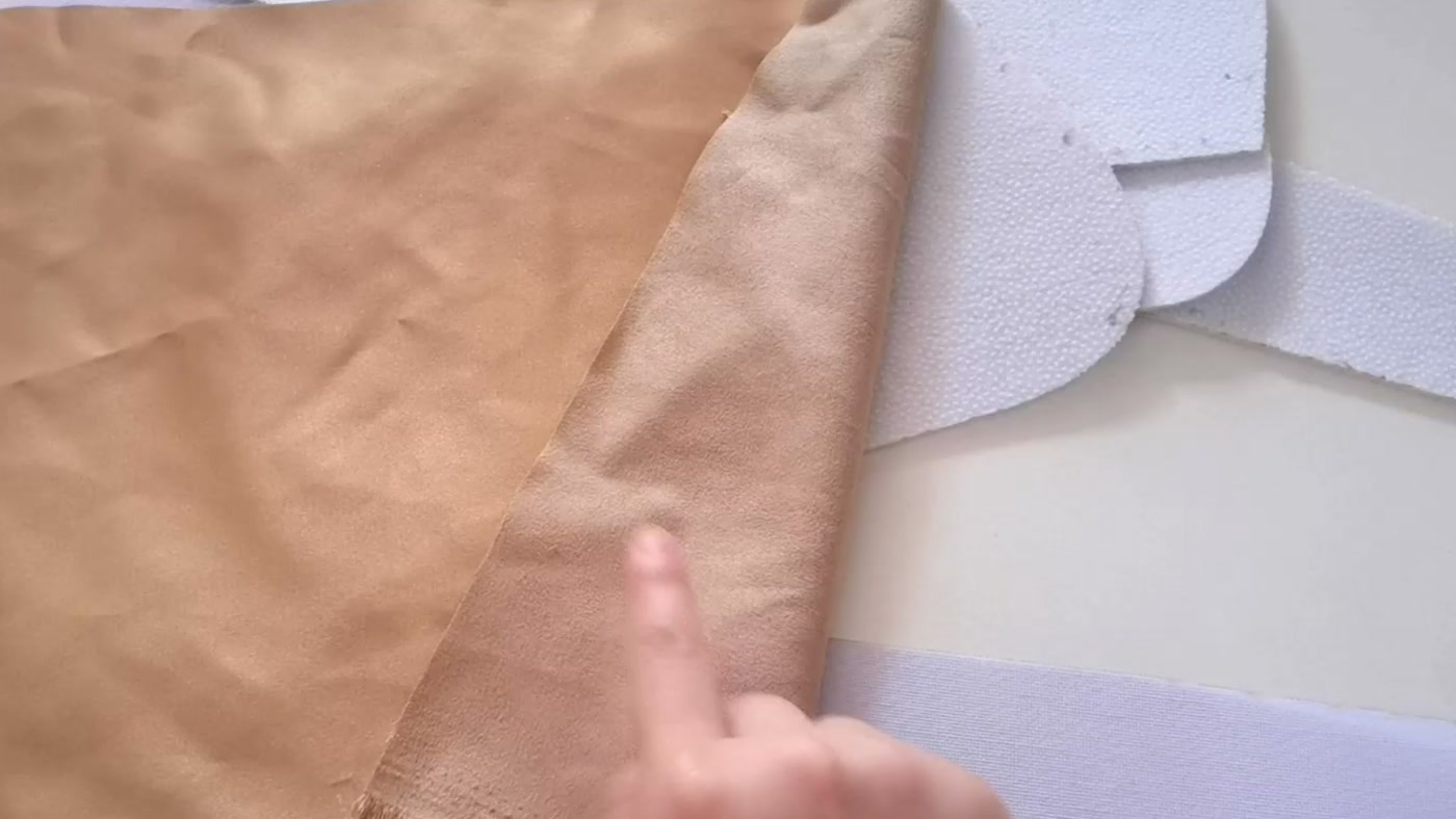 A hand indicating the wrong side of brown fabric beside the completed white stabilizer pieces