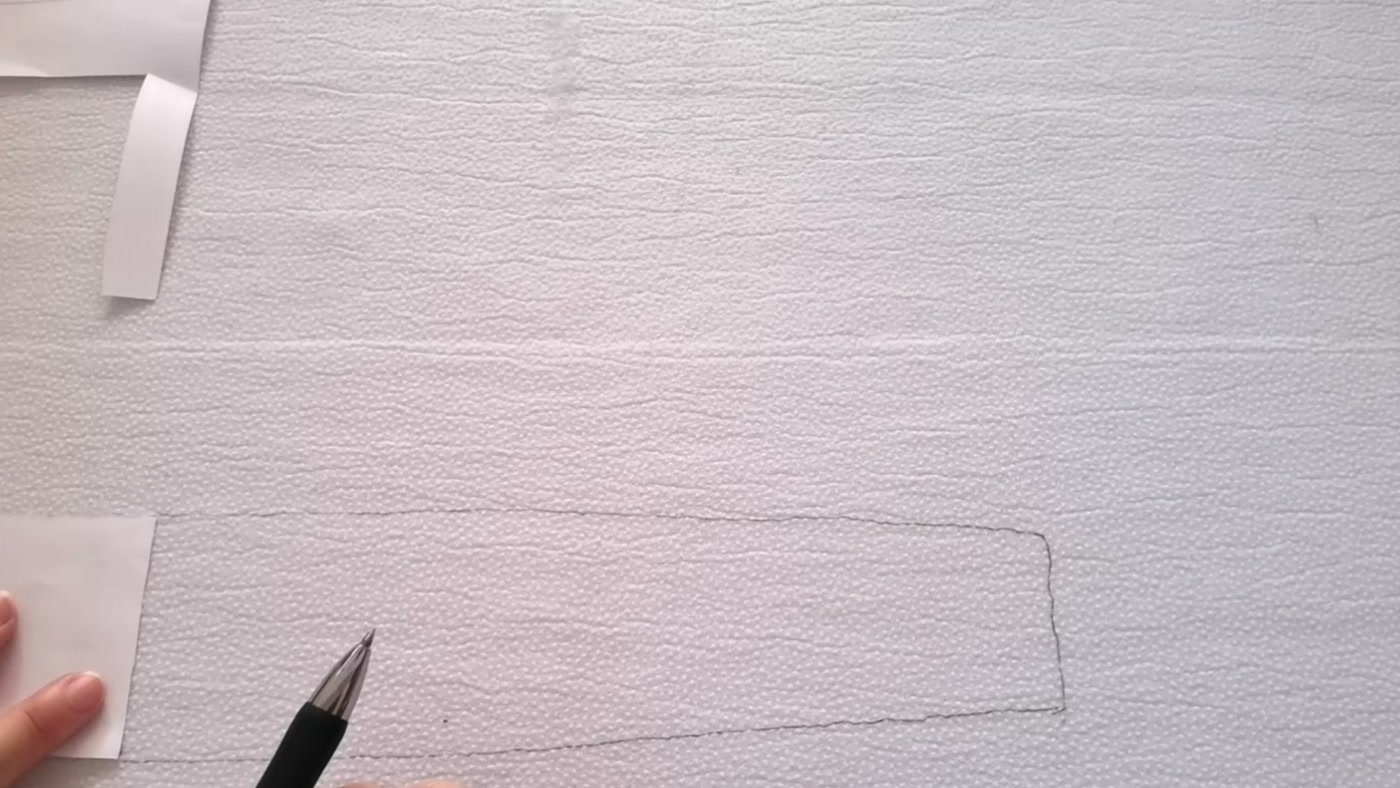 A pen tracing the edge of one paper half-pattern position before the template is flipped